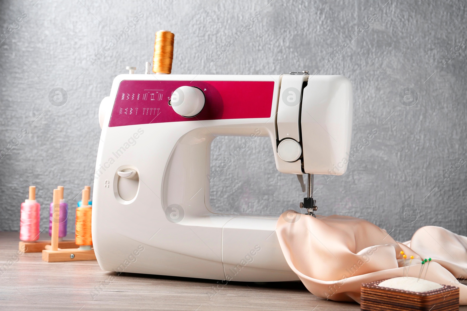 Photo of White sewing machine with beige fabric and craft accessories on wooden table near gray wall