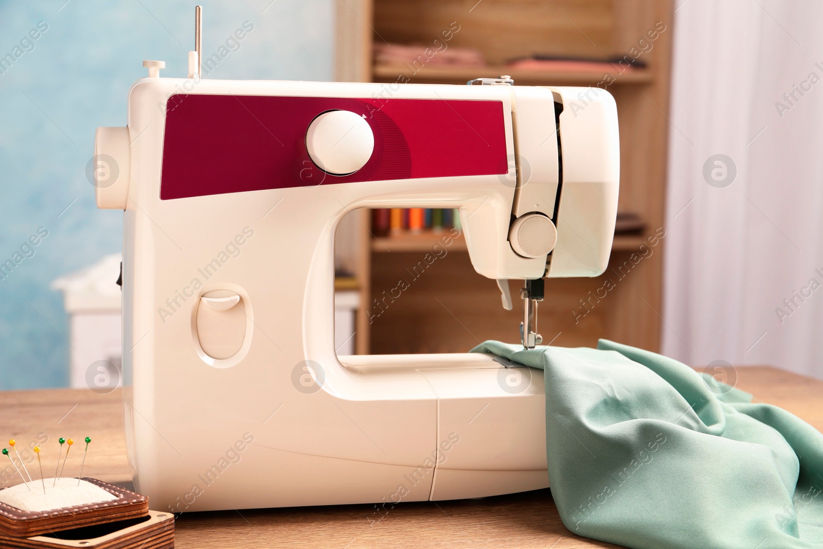 Photo of White sewing machine, color fabric and pin cushion with needles on wooden table indoors