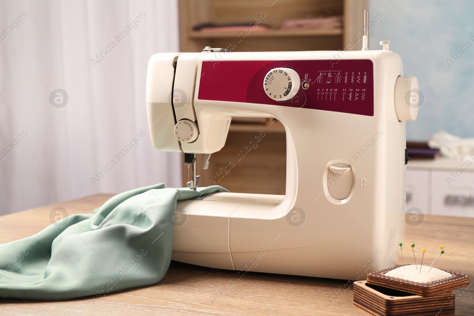 Photo of White sewing machine, color fabric and pin cushion with needles on wooden table indoors