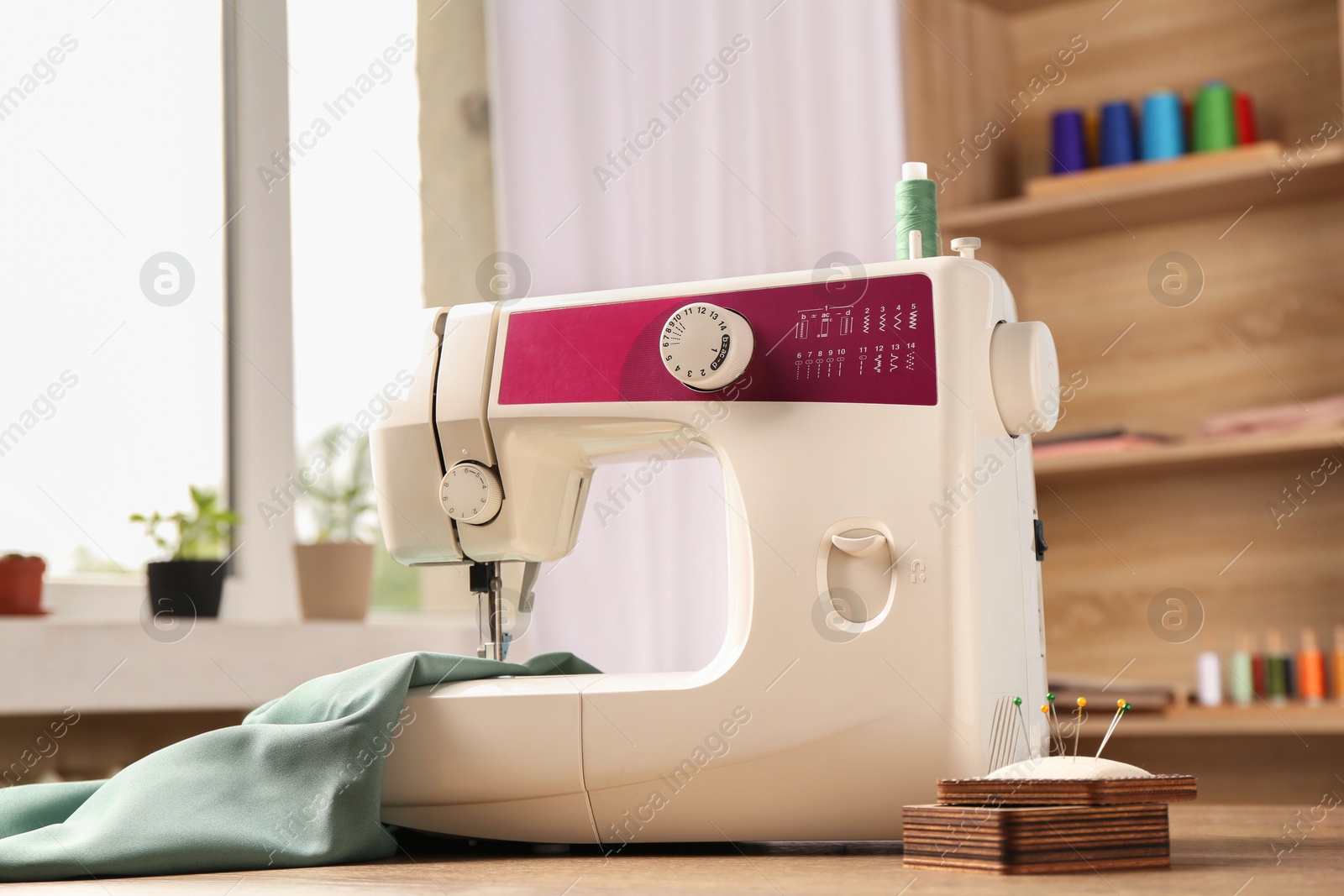 Photo of White sewing machine, color fabric and pin cushion with needles on wooden table indoors