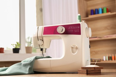 Photo of White sewing machine, color fabric and pin cushion with needles on wooden table indoors