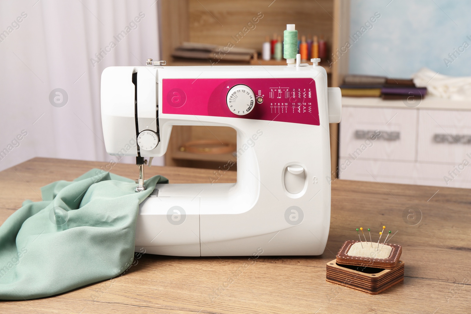 Photo of White sewing machine, color fabric and pin cushion with needles on wooden table indoors