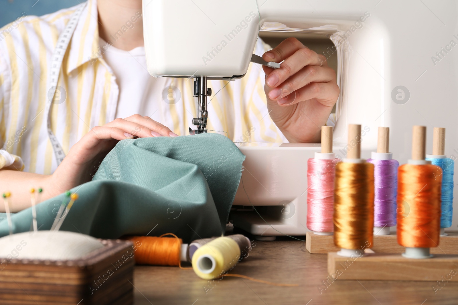 Photo of Seamstress working with sewing machine at wooden table indoors, closeup