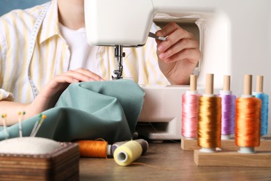 Seamstress working with sewing machine at wooden table indoors, closeup