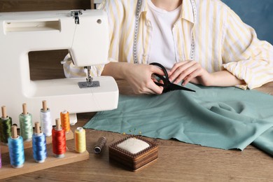 Photo of Seamstress cutting fabric at wooden table indoors, closeup