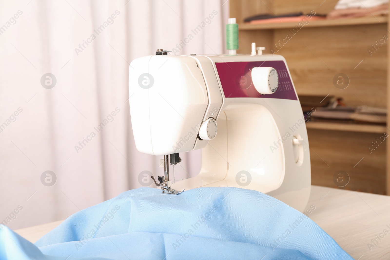 Photo of White sewing machine with light blue fabric on table indoors