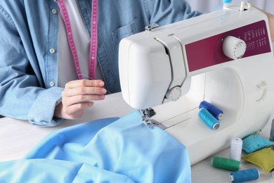 Seamstress working with sewing machine at table indoors, closeup