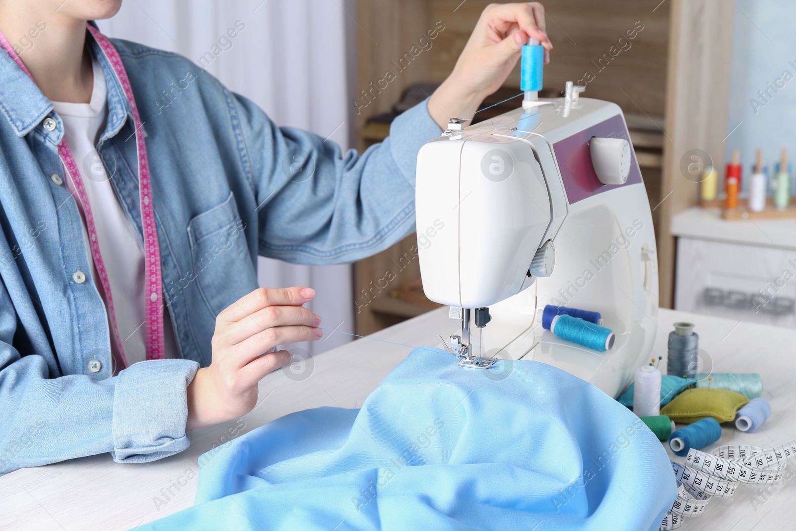 Photo of Seamstress working with sewing machine at white table indoors, closeup