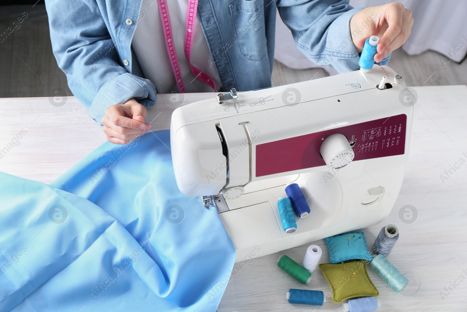 Photo of Seamstress working with sewing machine at white wooden table indoors