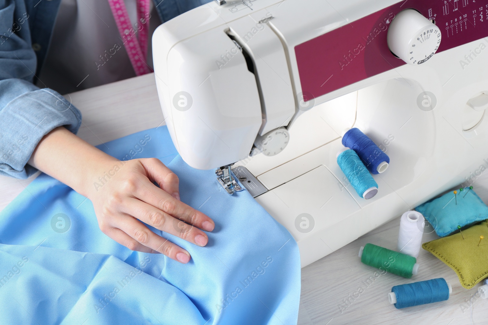 Photo of Seamstress working with sewing machine at white wooden table indoors, closeup