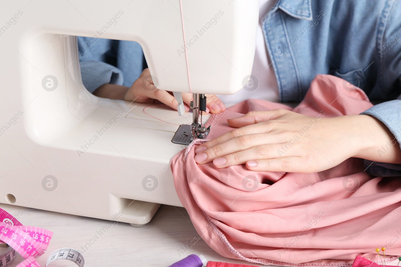 Photo of Seamstress working with sewing machine at white table indoors, closeup