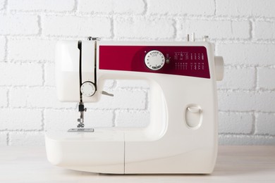 Photo of Modern sewing machine on wooden table near white brick wall