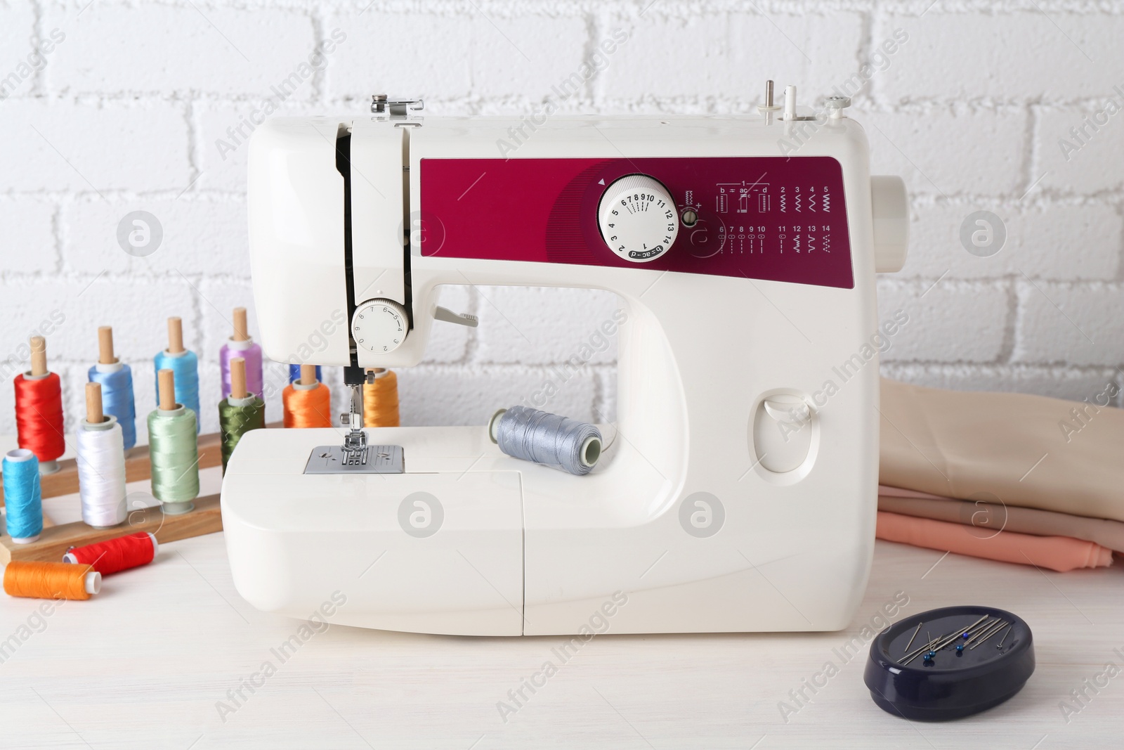 Photo of Modern sewing machine and craft accessories on wooden table near white brick wall