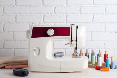 Photo of Modern sewing machine and craft accessories on wooden table near white brick wall