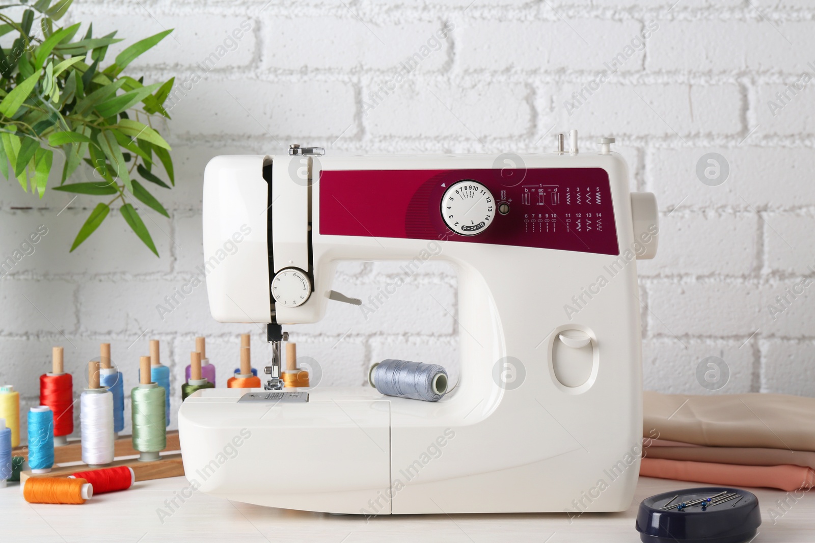 Photo of Modern sewing machine and craft accessories on wooden table near white brick wall