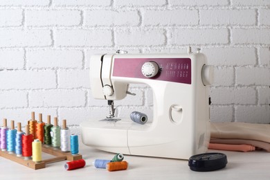 Photo of Modern sewing machine and craft accessories on wooden table near white brick wall