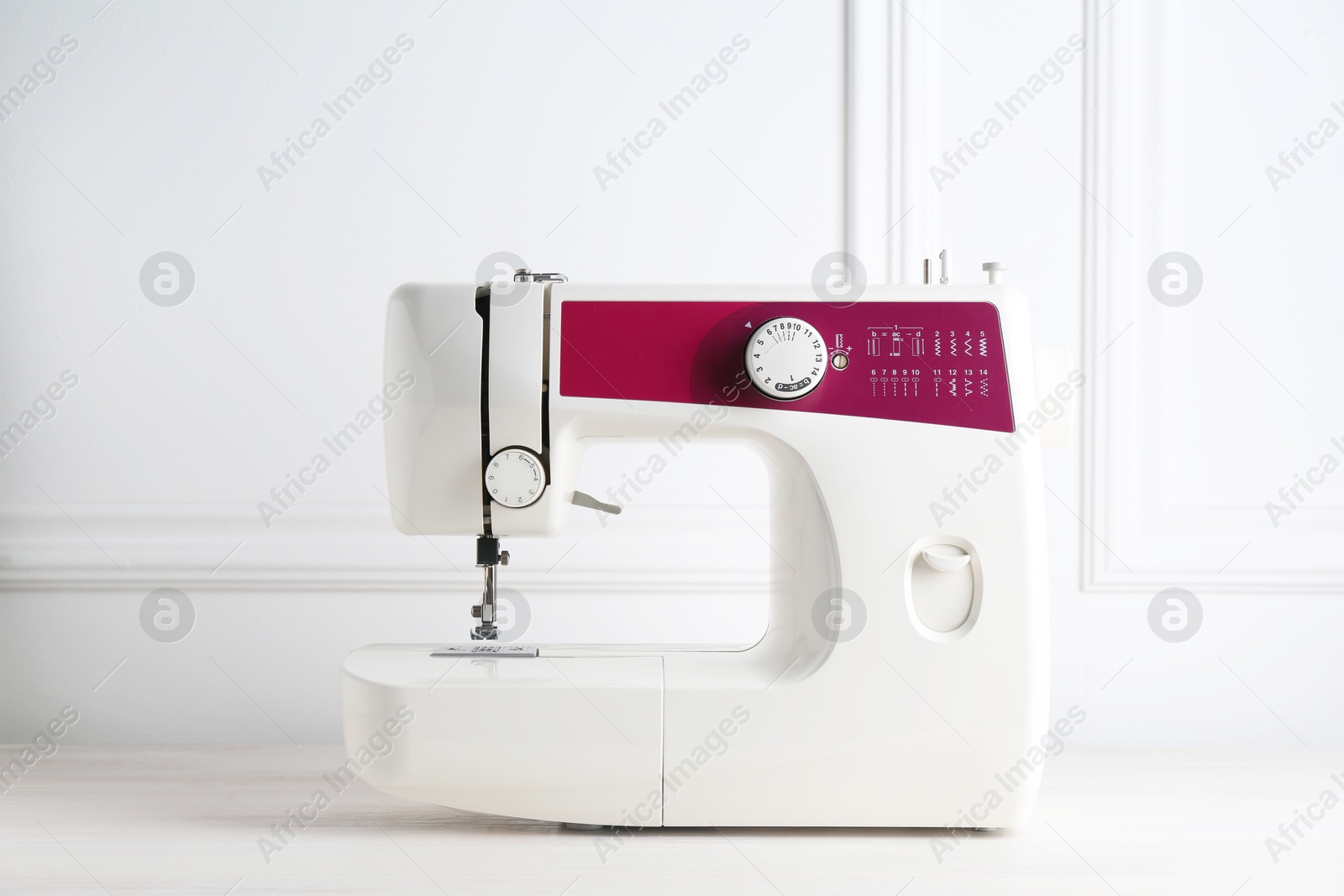 Photo of Modern sewing machine on white wooden table indoors