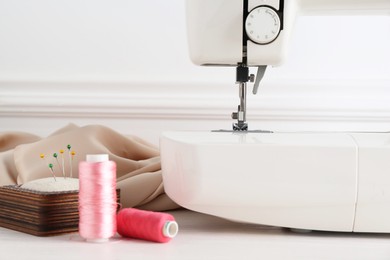 Photo of Sewing machine and craft accessories on white wooden table indoors, closeup