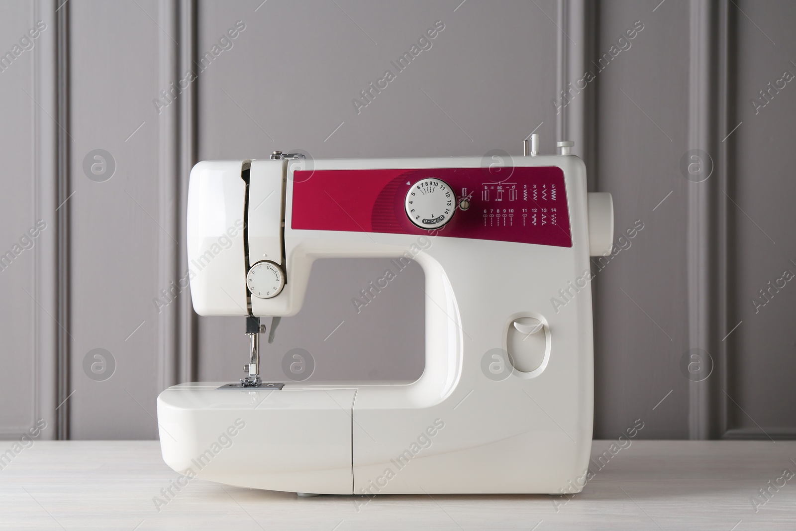 Photo of Sewing machine on white wooden table near gray wall