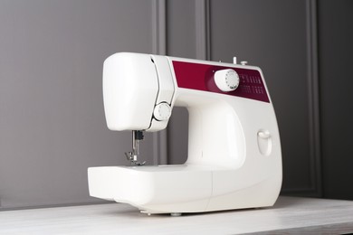 Photo of Sewing machine on white wooden table near gray wall