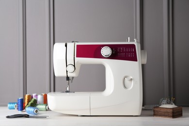 Photo of Sewing machine and craft accessories on white wooden table near gray wall