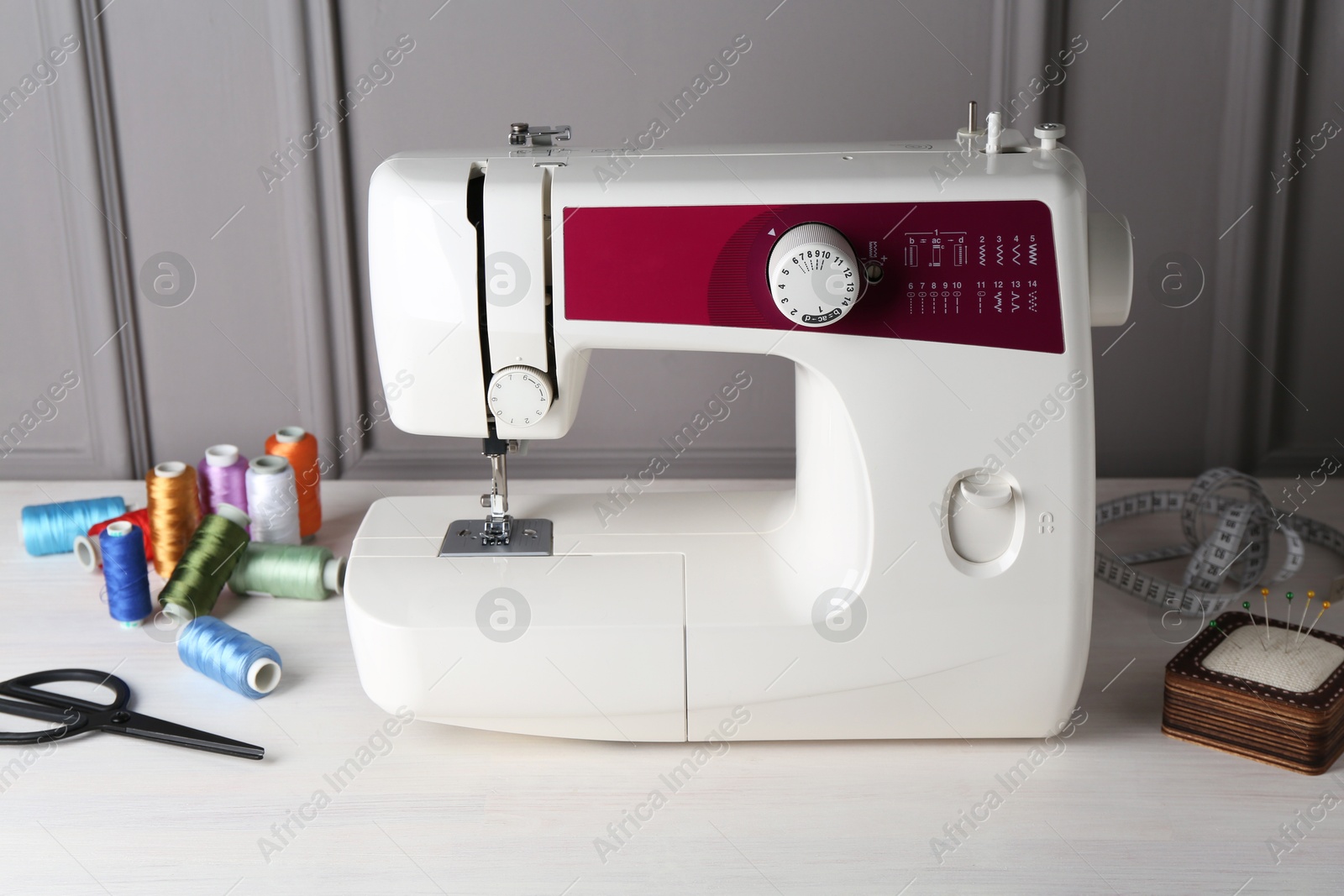 Photo of Sewing machine and craft accessories on white wooden table near gray wall