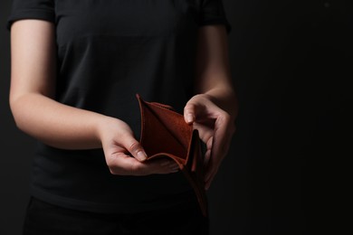 Photo of Woman with empty wallet on dark background, closeup. Space for text