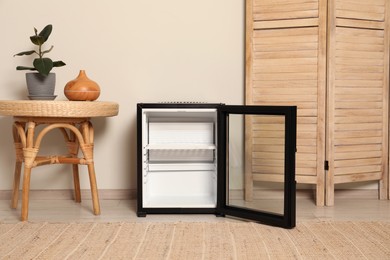 Photo of Empty modern mini refrigerator near beige wall indoors