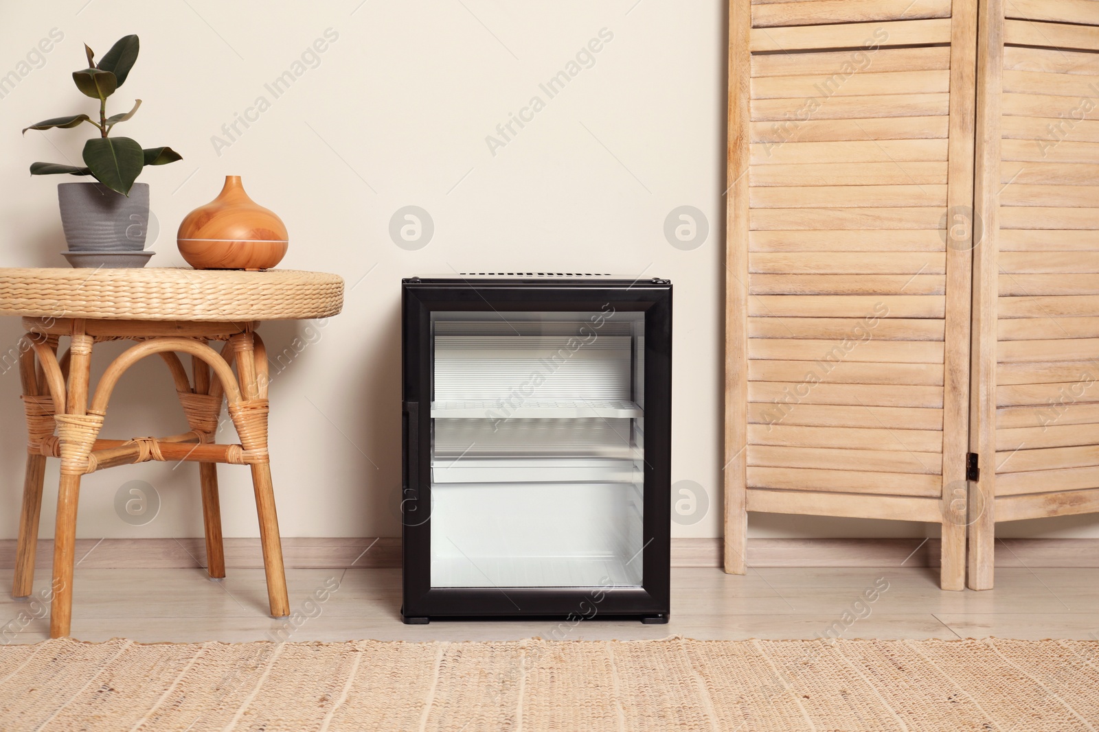 Photo of Empty modern mini refrigerator near beige wall indoors