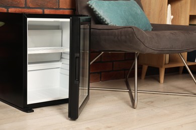 Photo of Empty modern mini refrigerator near chair indoors, closeup