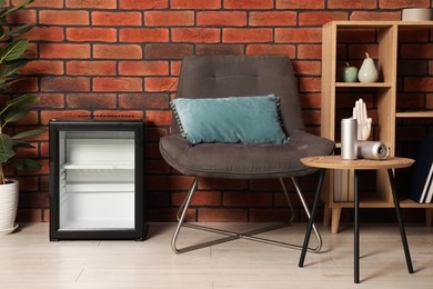 Photo of Empty modern mini refrigerator near chair indoors