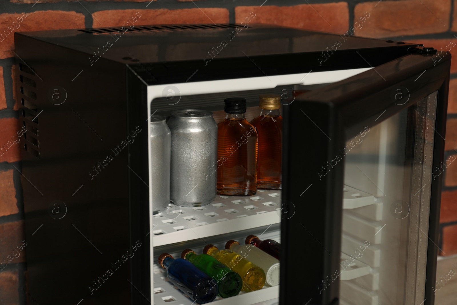 Photo of Mini refrigerator with drinks near brick wall, closeup