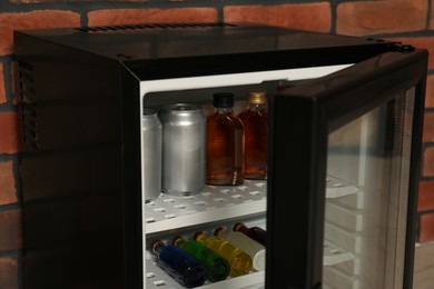 Mini refrigerator with drinks near brick wall, closeup