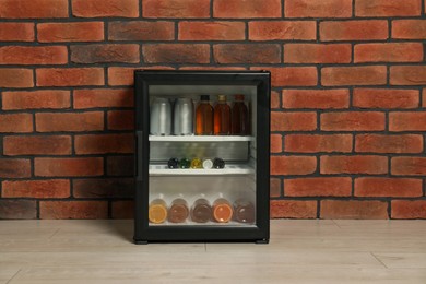 Mini refrigerator with drinks near brick wall