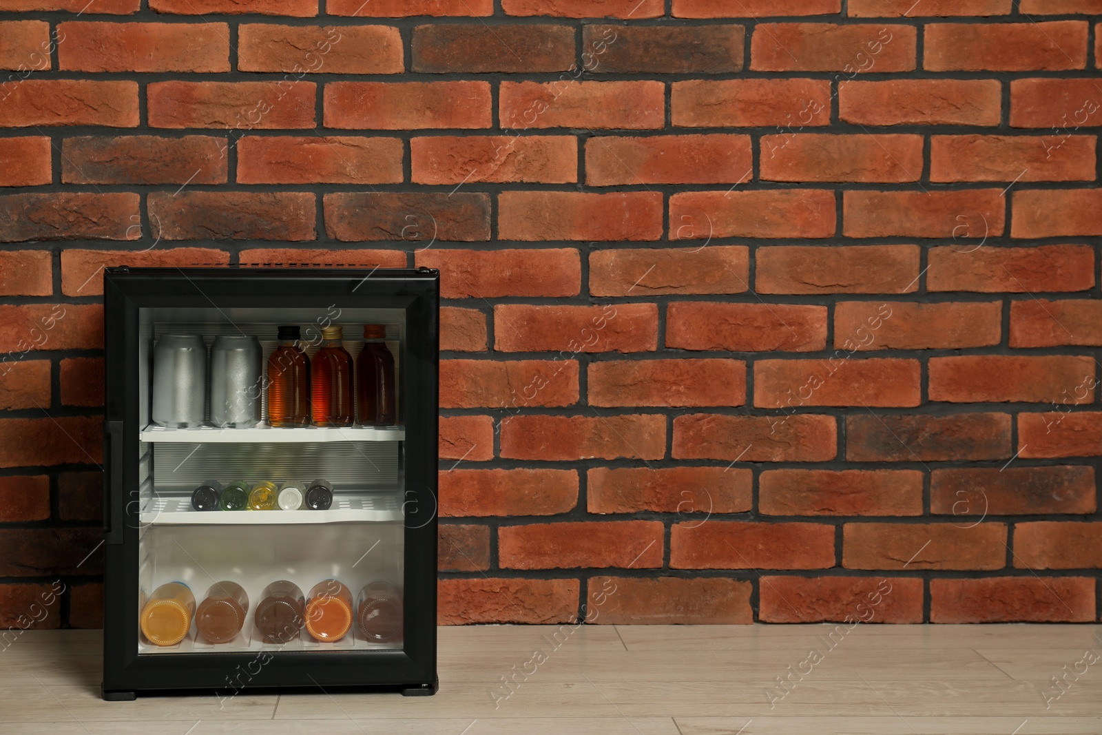 Photo of Mini refrigerator with drinks near brick wall. Space for text