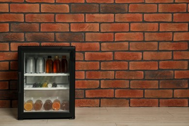 Mini refrigerator with drinks near brick wall. Space for text