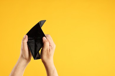 Photo of Man with empty wallet on yellow background, closeup. Space for text