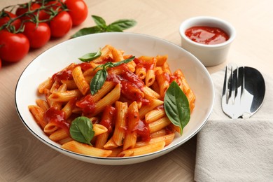 Delicious pasta with tomato sauce and basil in bowl served on wooden table, closeup