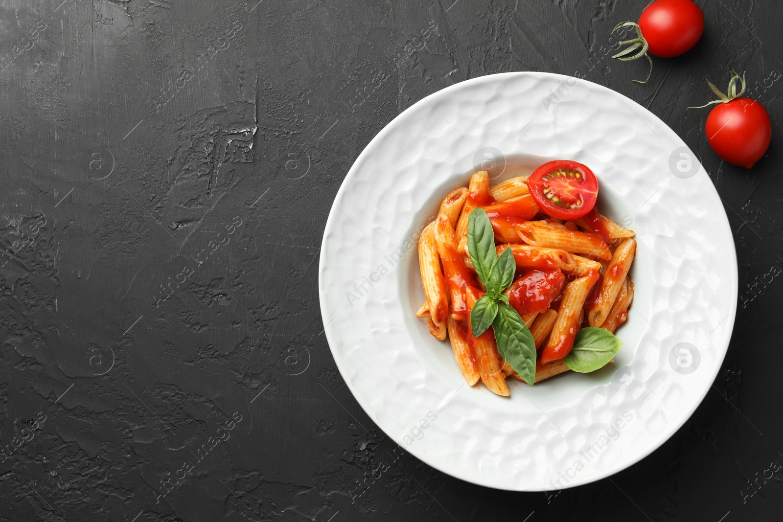 Photo of Delicious pasta with tomato sauce and basil on black textured table, flat lay. Space for text