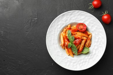 Photo of Delicious pasta with tomato sauce and basil on black textured table, flat lay. Space for text