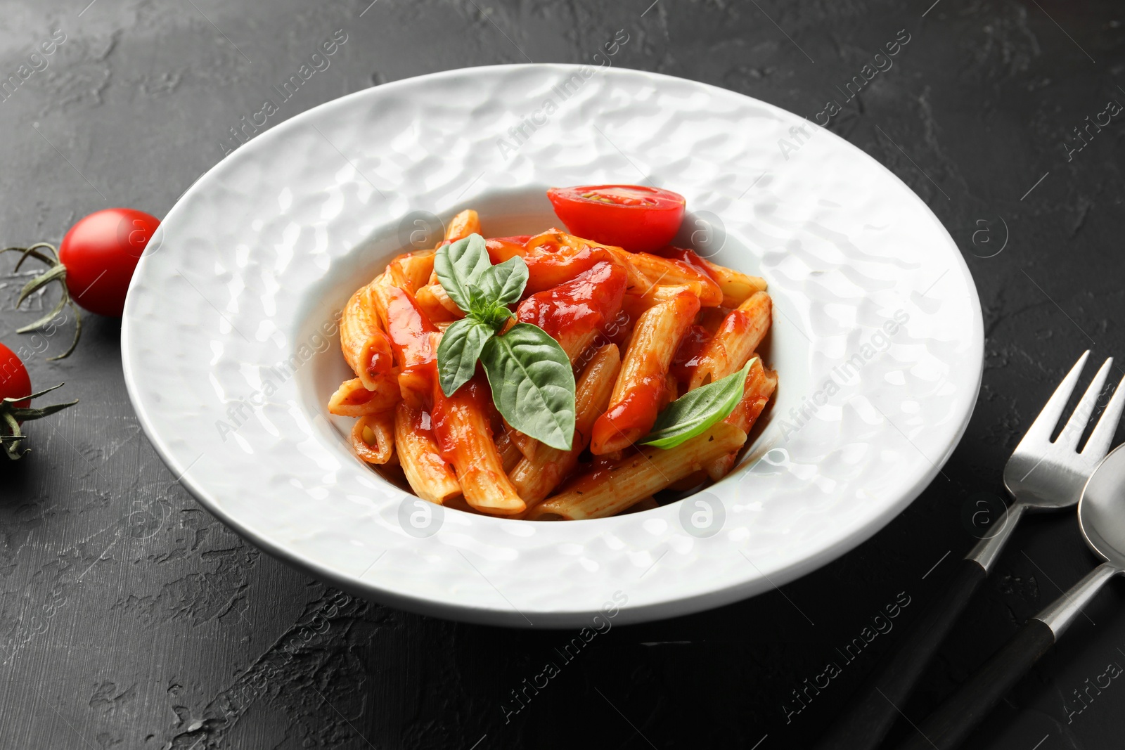 Photo of Delicious pasta with tomato sauce and basil served on black textured table