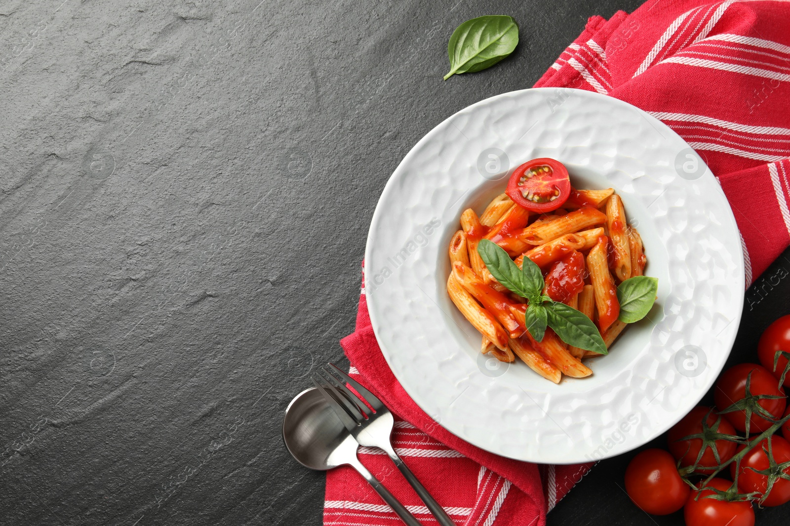 Photo of Delicious pasta with tomato sauce and basil served on black textured table, flat lay. Space for text