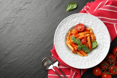 Delicious pasta with tomato sauce and basil served on black textured table, flat lay. Space for text