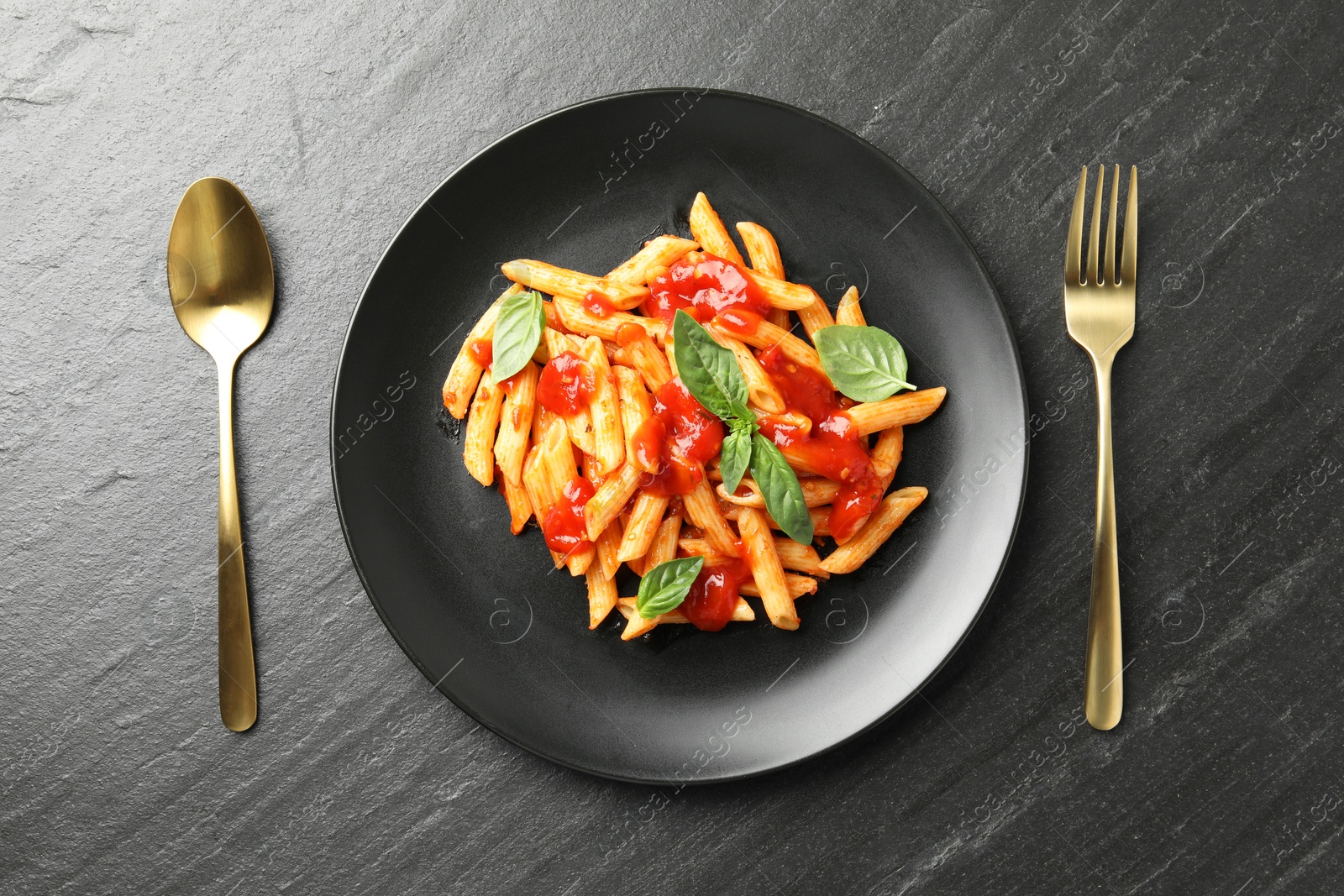 Photo of Delicious pasta with tomato sauce and basil served on black textured table, flat lay