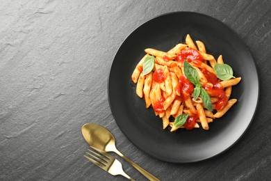 Photo of Delicious pasta with tomato sauce and basil served on black textured table, flat lay. Space for text