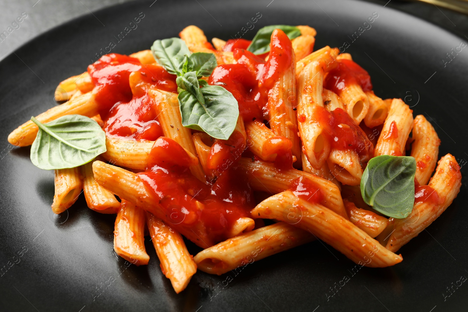 Photo of Delicious pasta with tomato sauce and basil on black plate, closeup