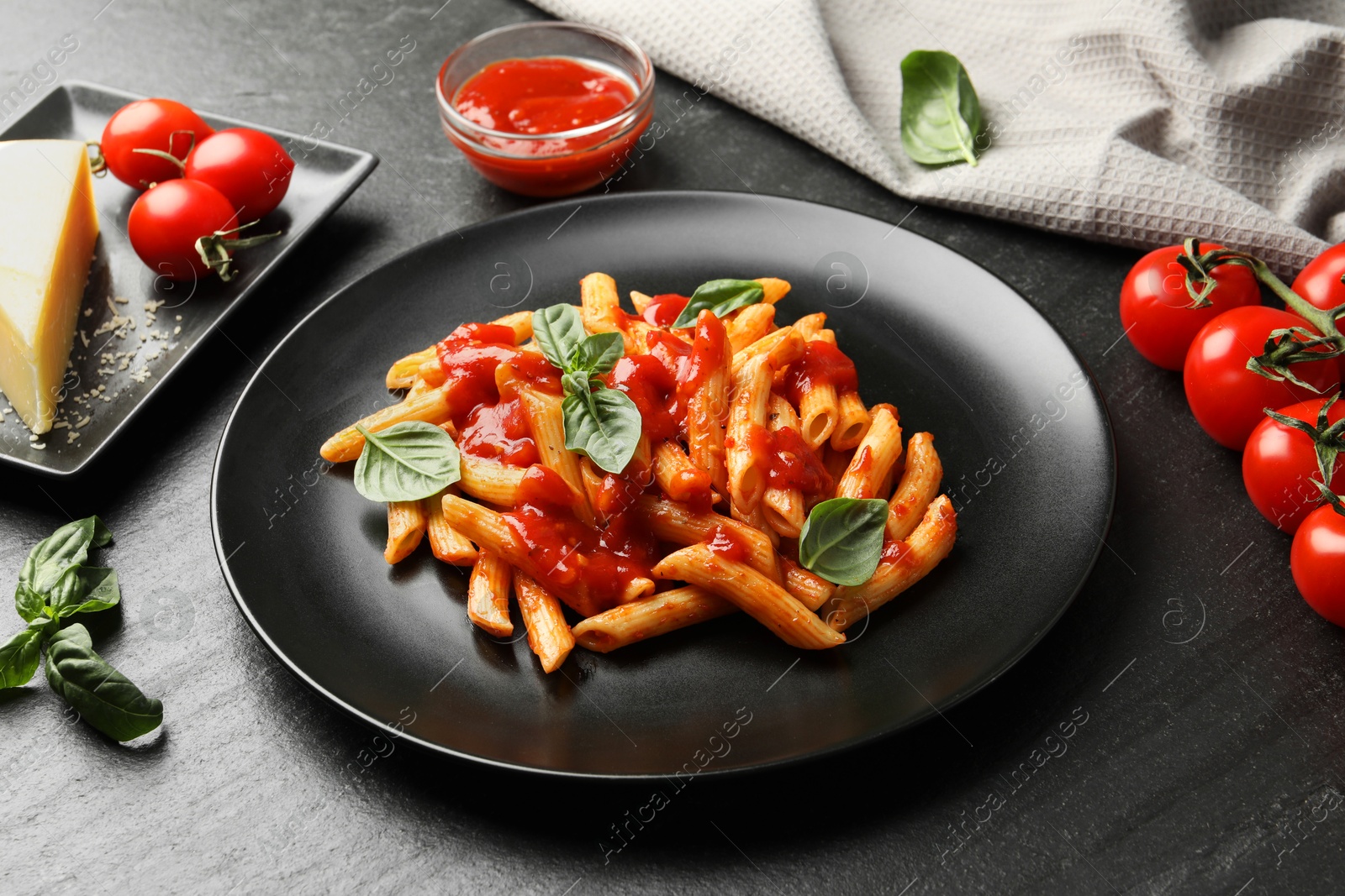 Photo of Delicious pasta with tomato sauce, basil and cheese on black textured table