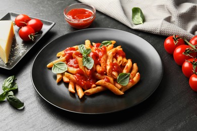 Delicious pasta with tomato sauce, basil and cheese on black textured table