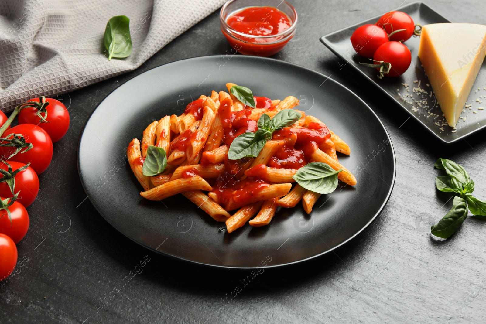 Photo of Delicious pasta with tomato sauce, basil and cheese on black textured table