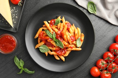 Photo of Delicious pasta with tomato sauce, basil and cheese on black textured table, flat lay